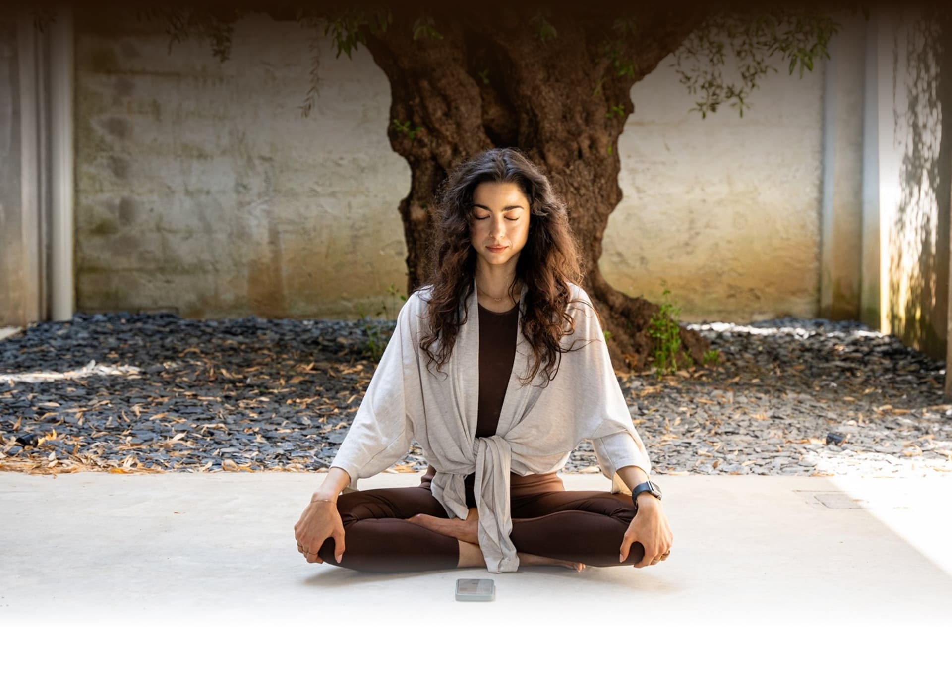 Woman meditating peacefully under a tree in a serene outdoor setting